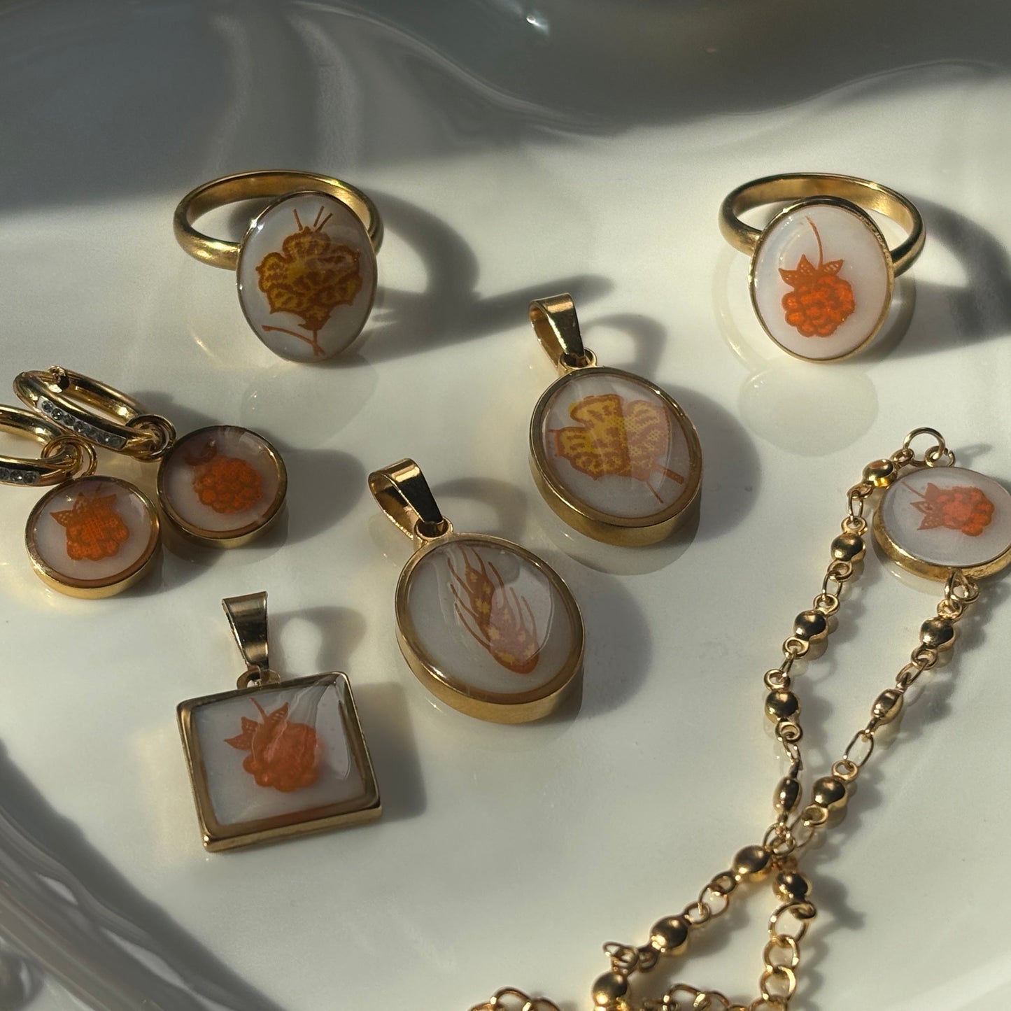 A collection of gold-toned jewelry pieces featuring carved orange and white shell inlays, arranged on a white ceramic dish.