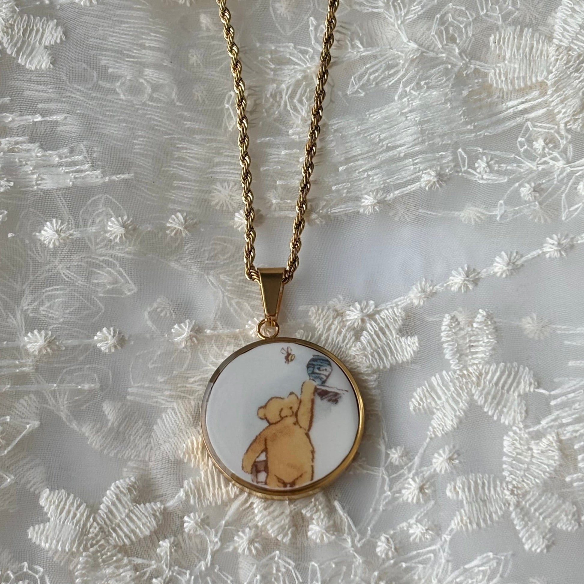 Gold necklace with a round pendant featuring a bear illustration on a textured white background