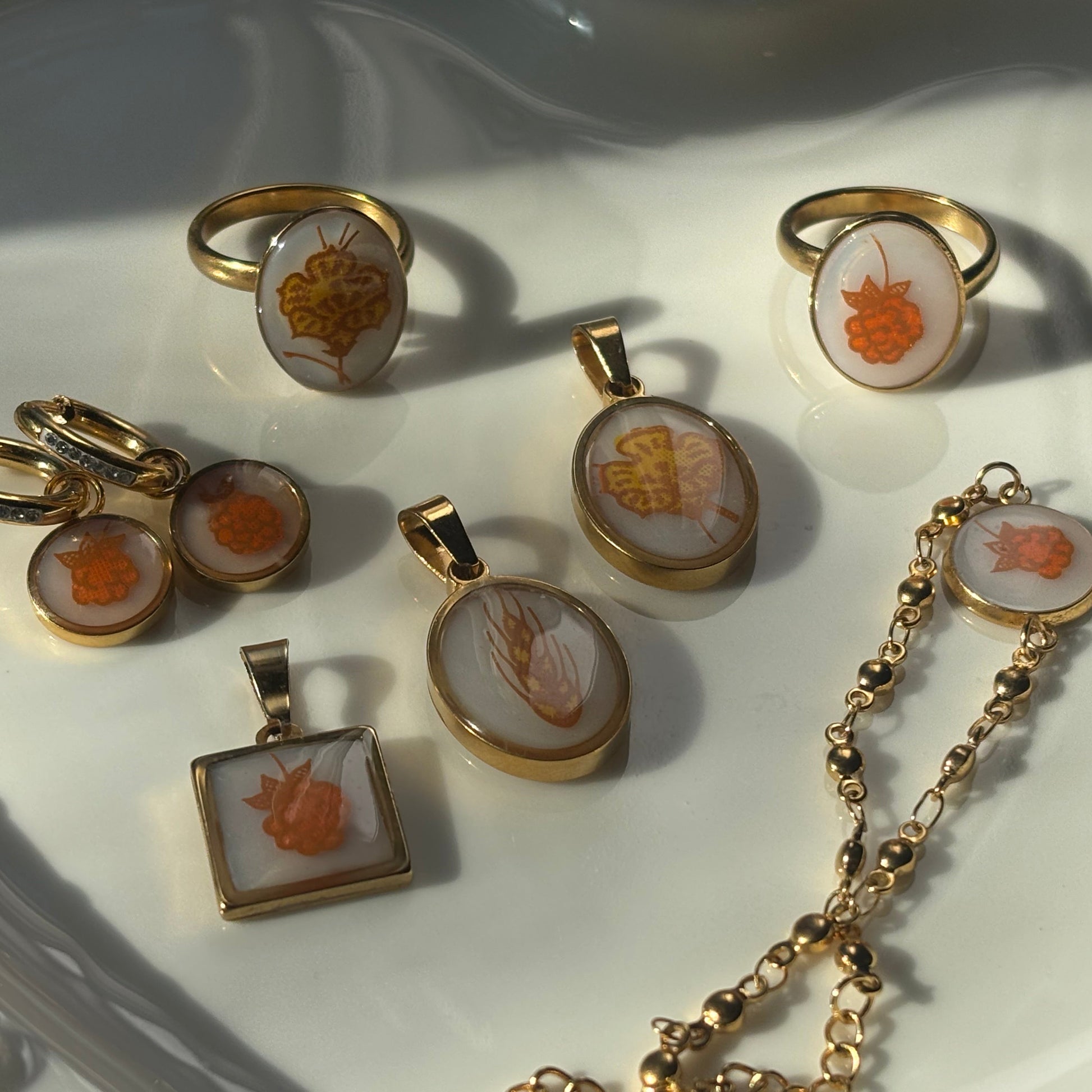 A collection of gold-toned jewelry pieces featuring carved orange and white shell inlays, arranged on a white ceramic dish.