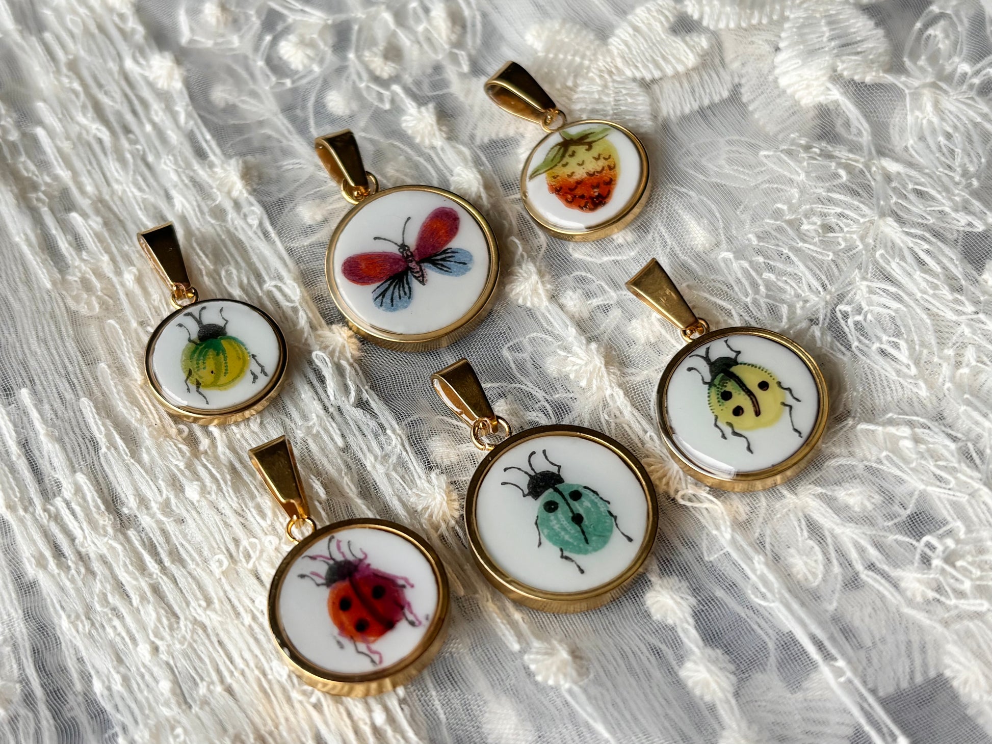 Set of six small round pendants with insect designs on a lace background
