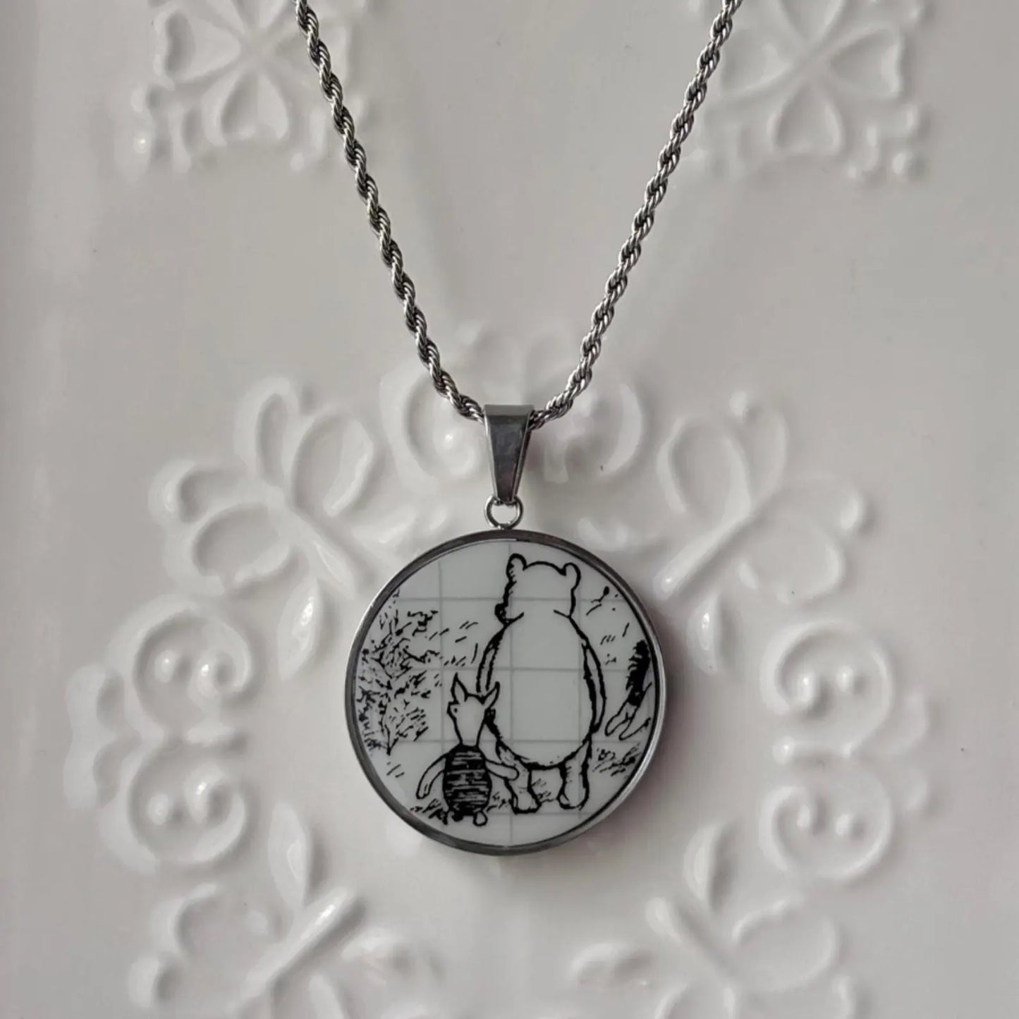 Necklace with a round pendant featuring a bear and rabbit design on an embossed white background.