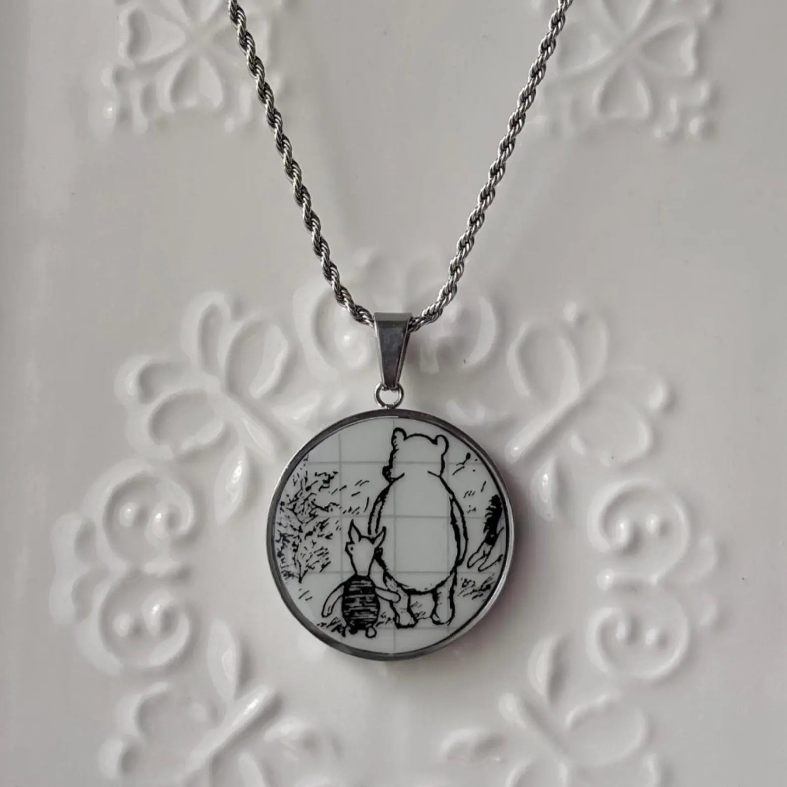 Necklace with a round pendant featuring a bear and rabbit design on an embossed white background.