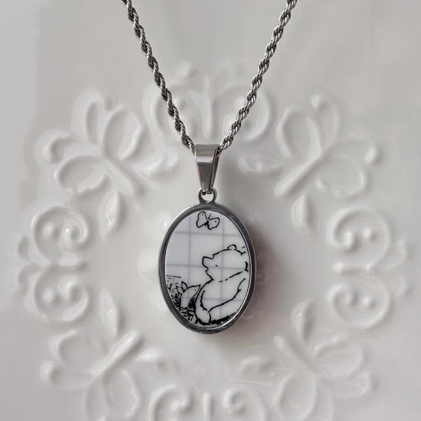 Silver pendant with a black and white design on a textured white background