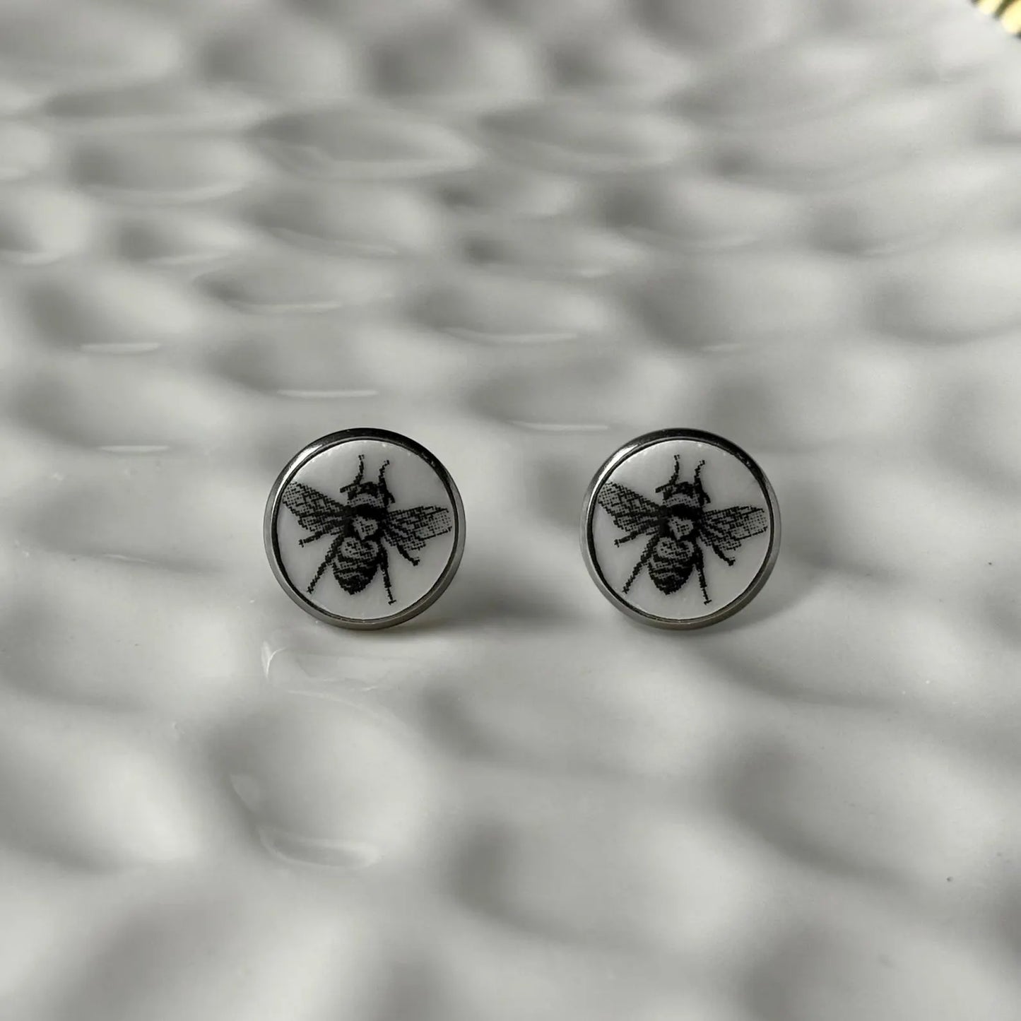 Round earrings with bee design on a textured gray background