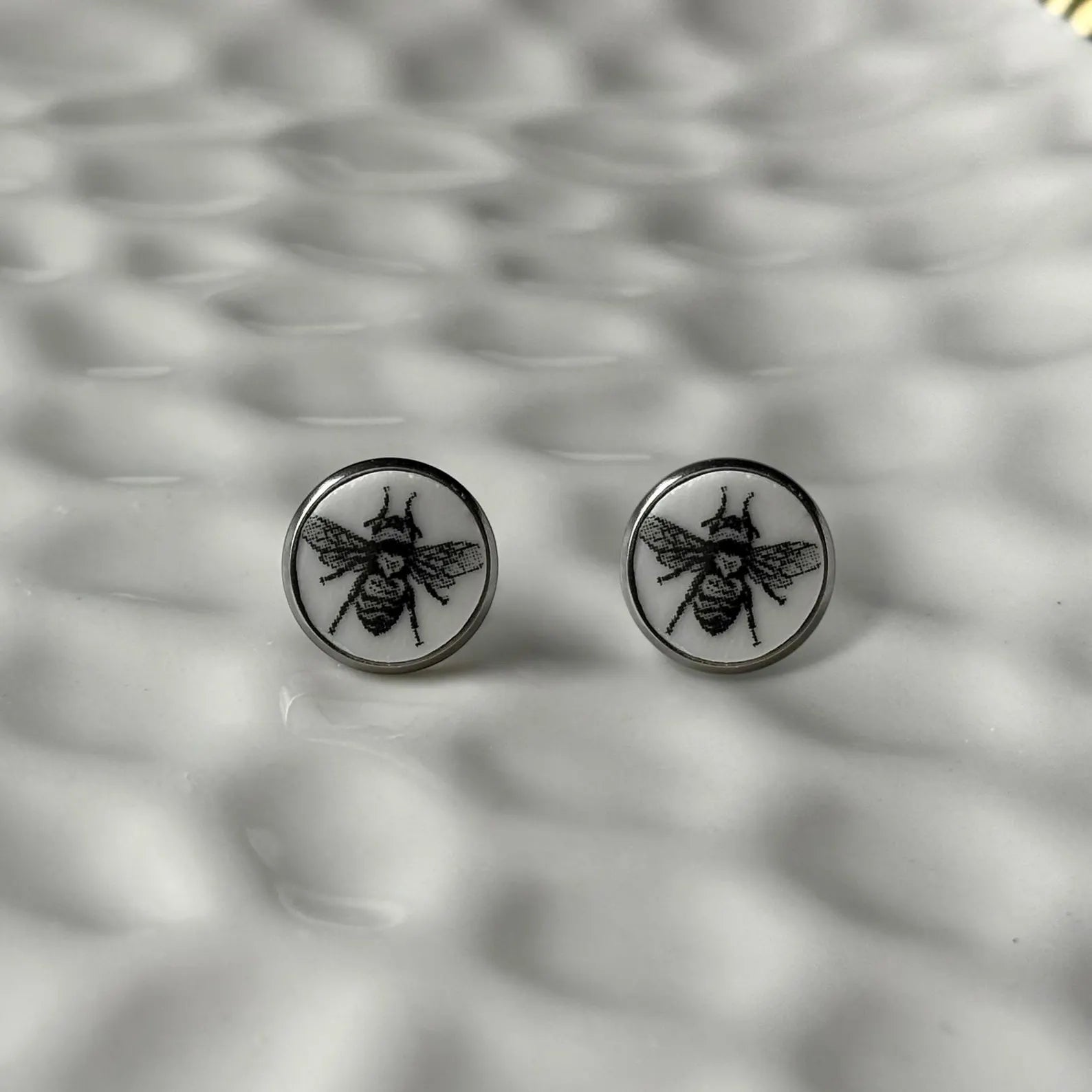 Round earrings with bee design on a textured gray background