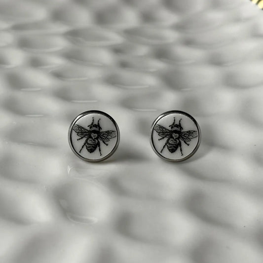 Round earrings with bee design on a textured gray background