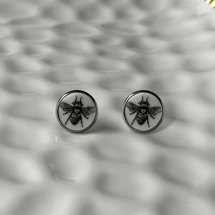 Round earrings with bee design on a textured gray background