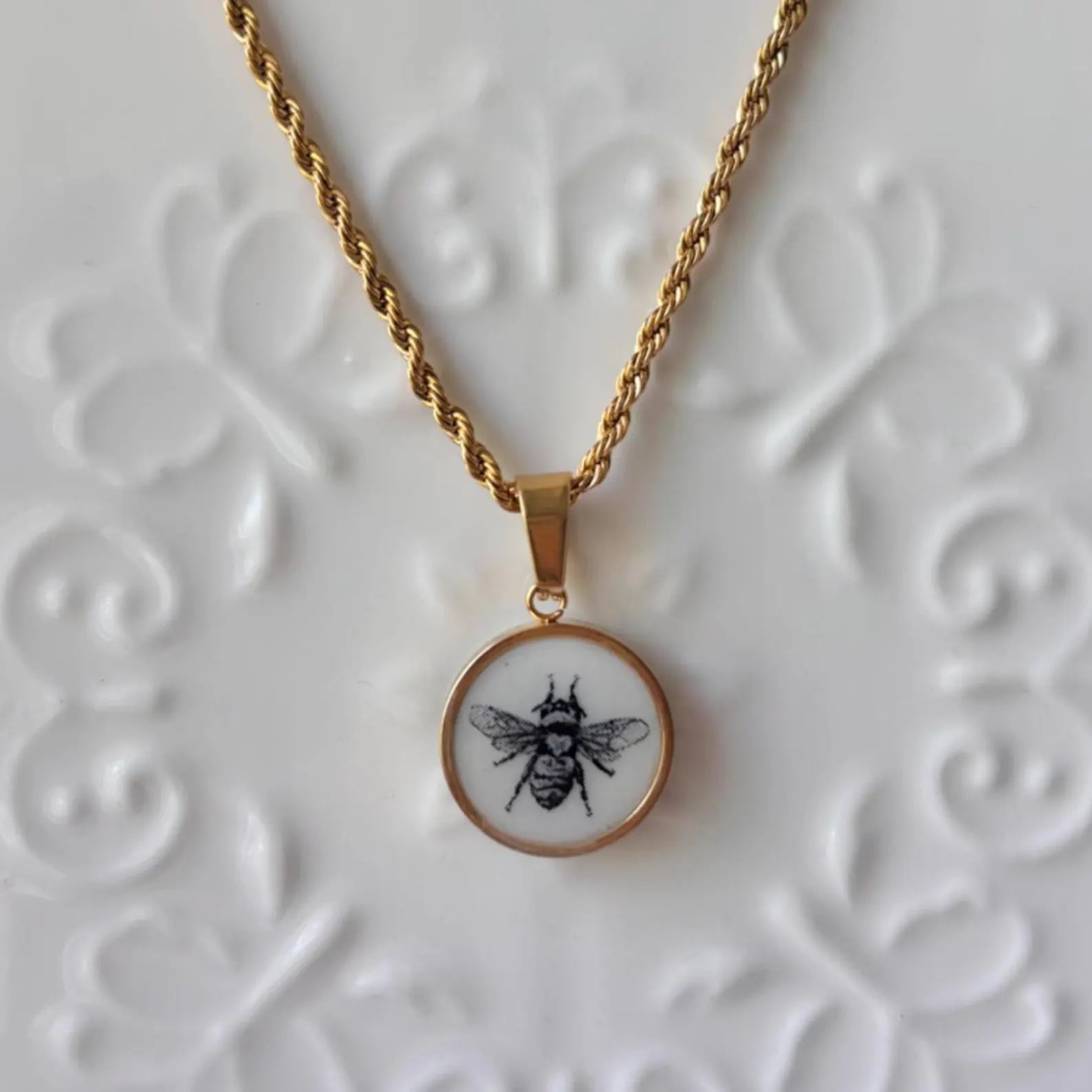 Necklace with a pendant featuring a bee design on a textured white background