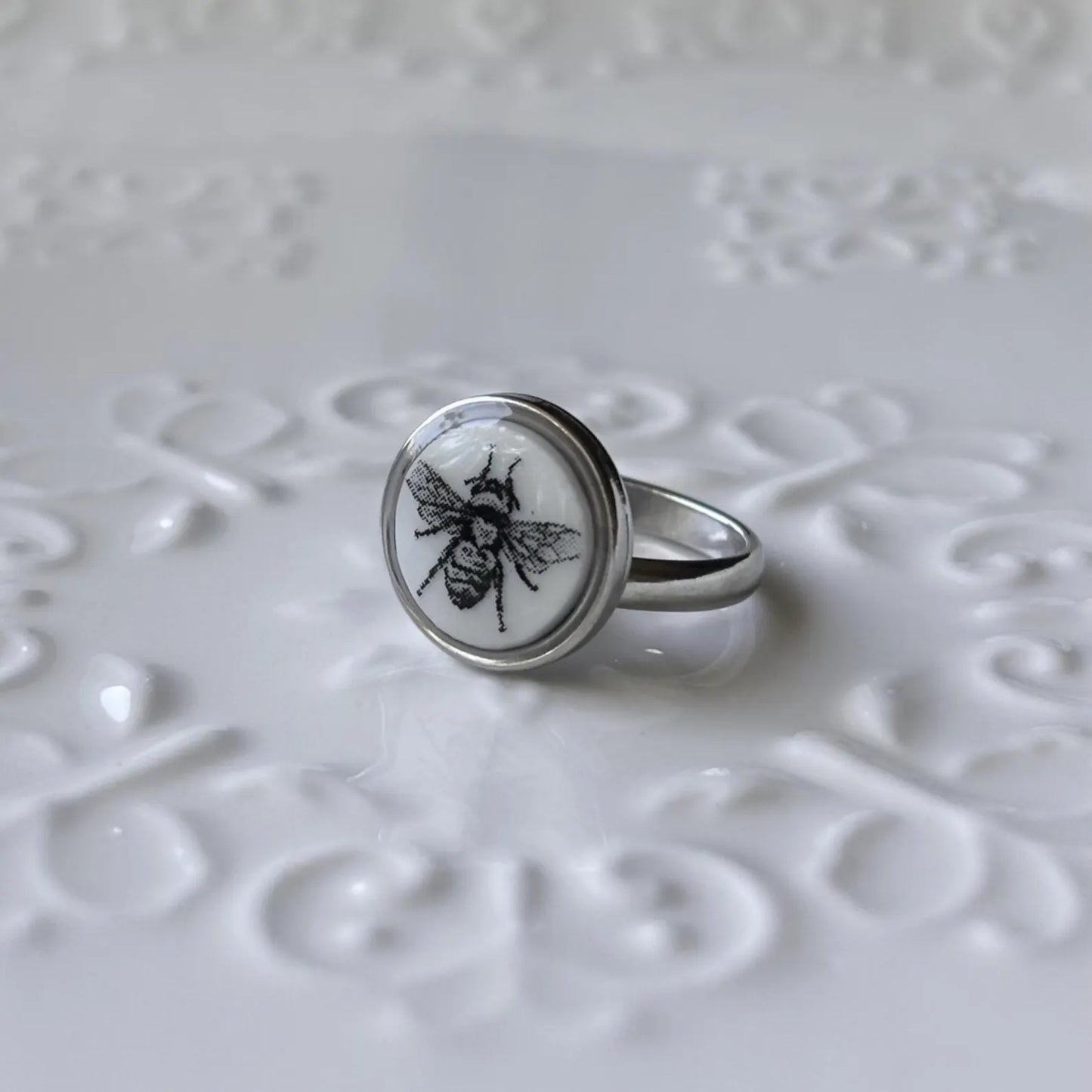 Silver ring with a bee design on a textured white surface
