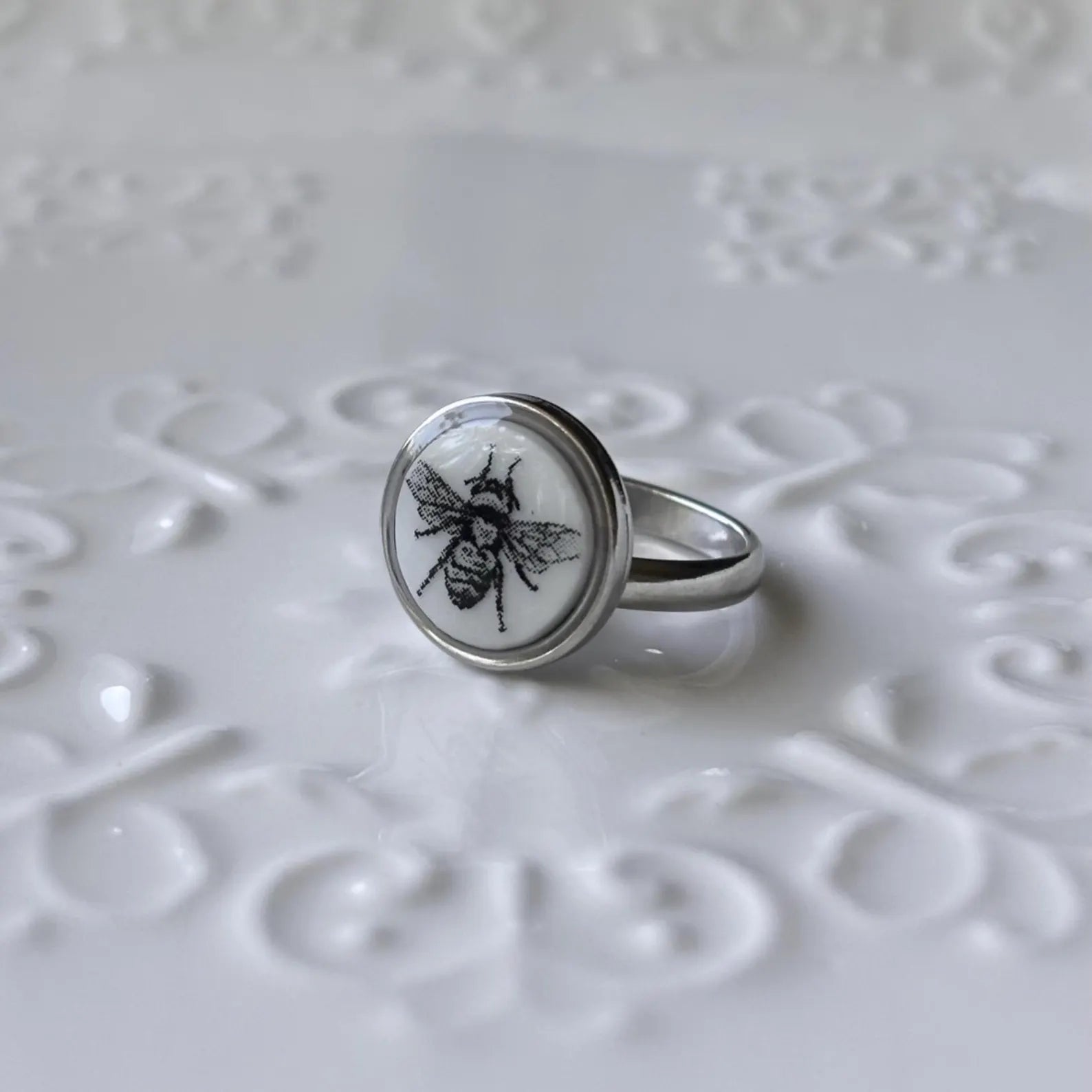 Silver ring with a bee design on a textured white surface