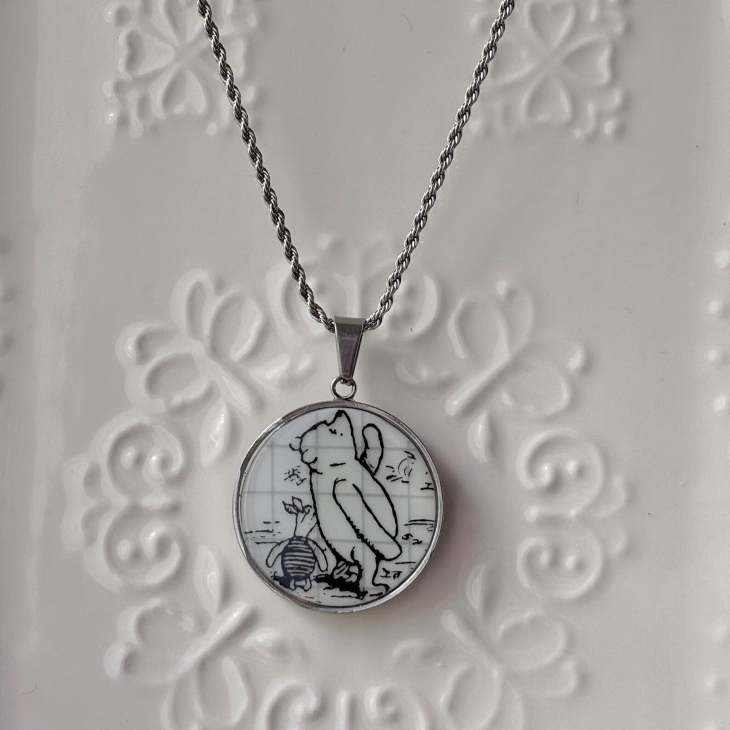 Necklace with a pendant featuring a cat and mouse design on a textured white background