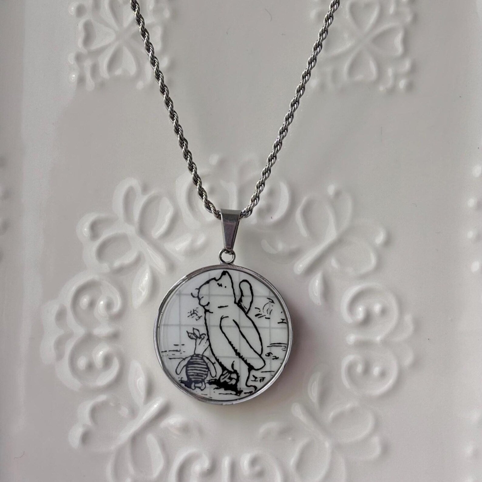 Necklace with a pendant featuring a cat and mouse design on a textured white background
