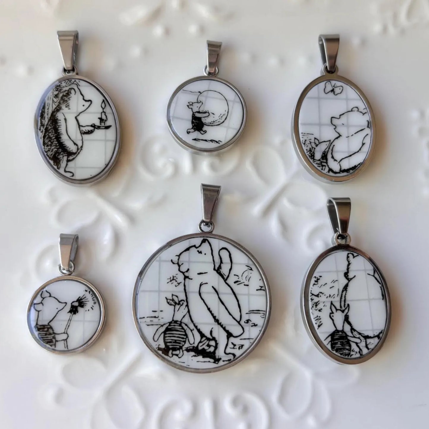 Set of six pendant necklaces with black and white illustrations on a textured white background