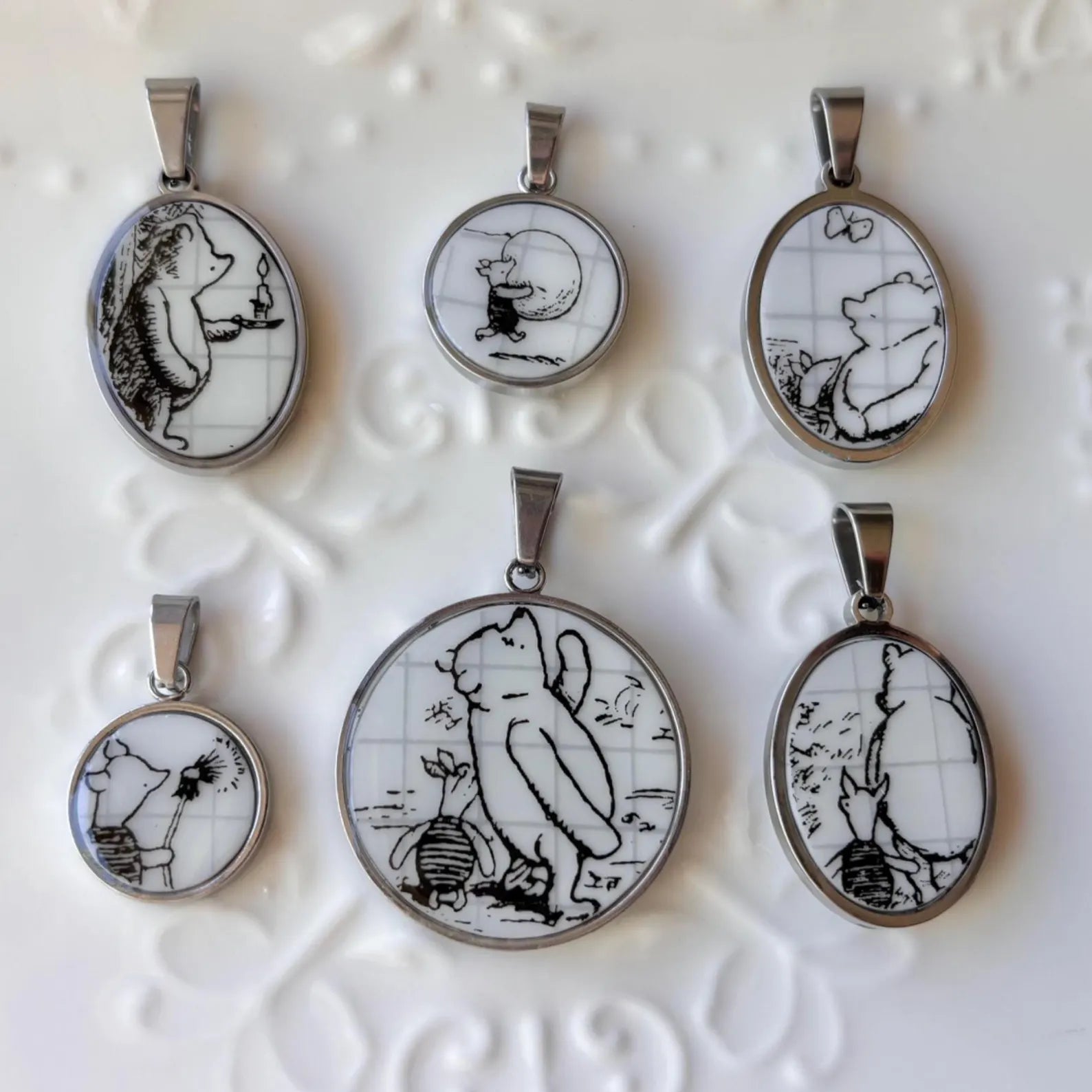 Set of six pendant necklaces with black and white illustrations on a textured white background