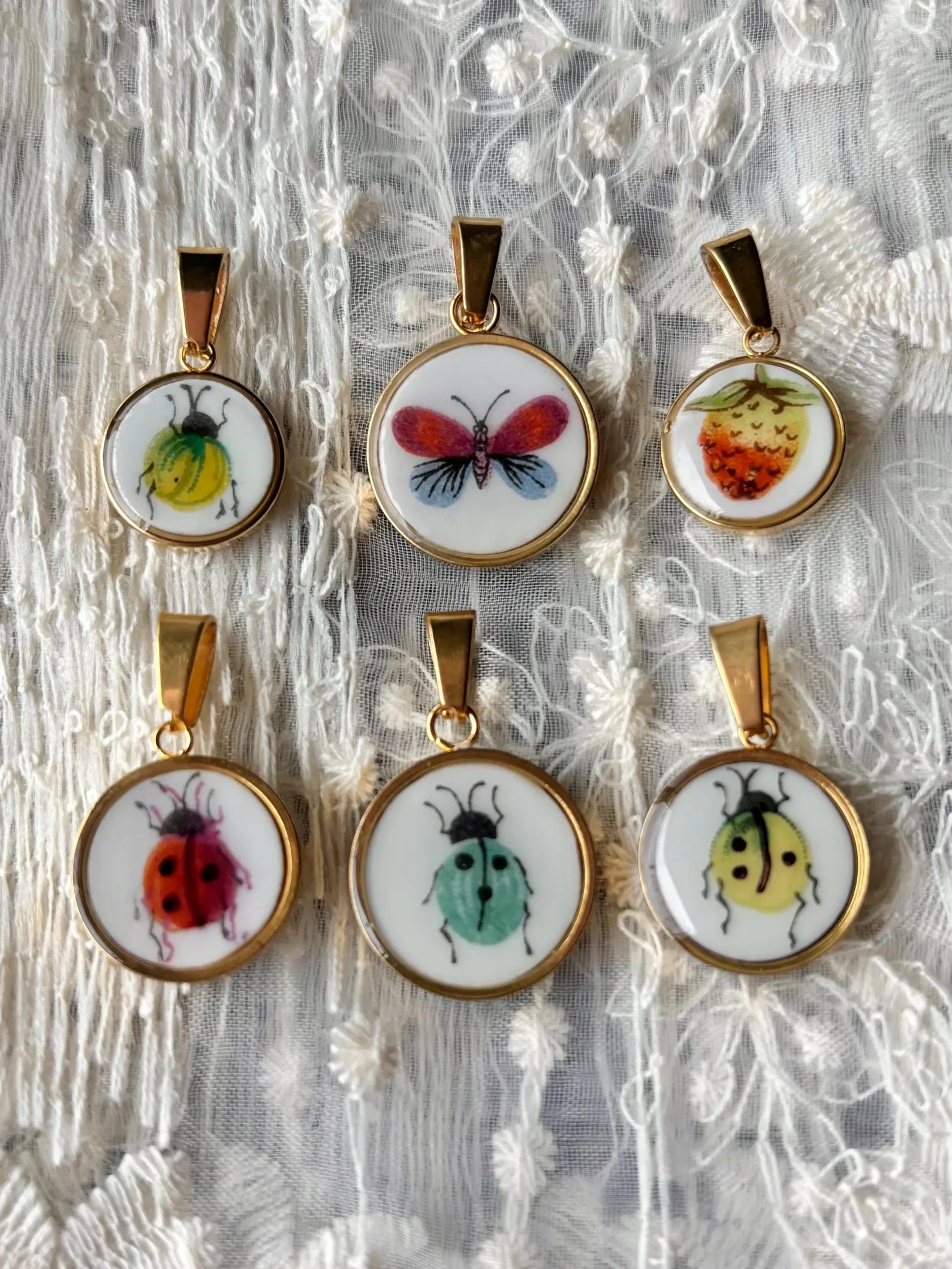 Set of six insect-themed pendants on a textured white background