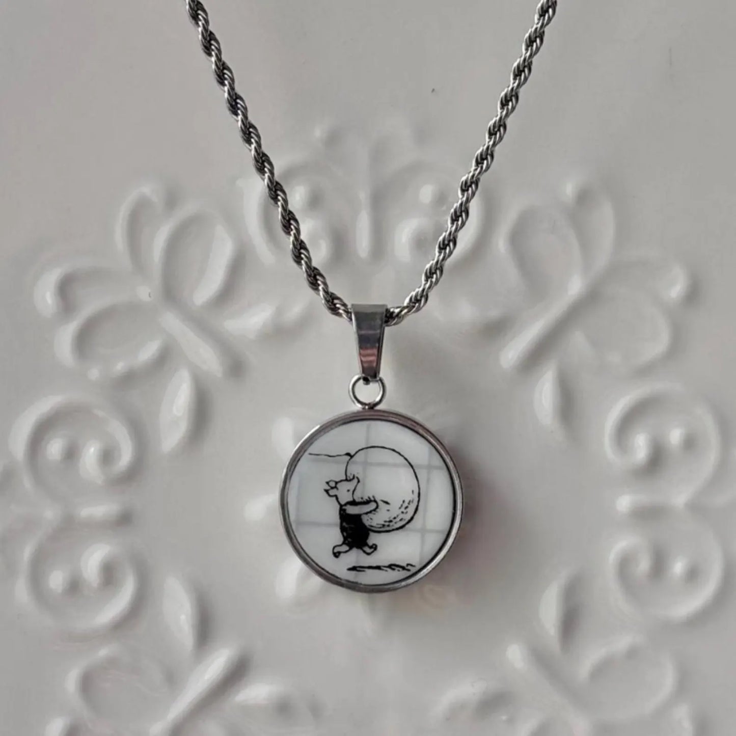 Necklace with a pendant featuring a black and white illustration on a textured gray background