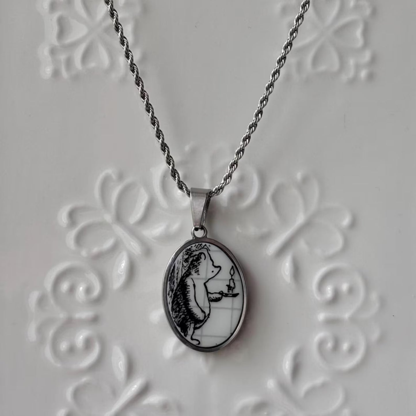 Silver necklace with a pendant featuring a black and white illustration on a textured gray background