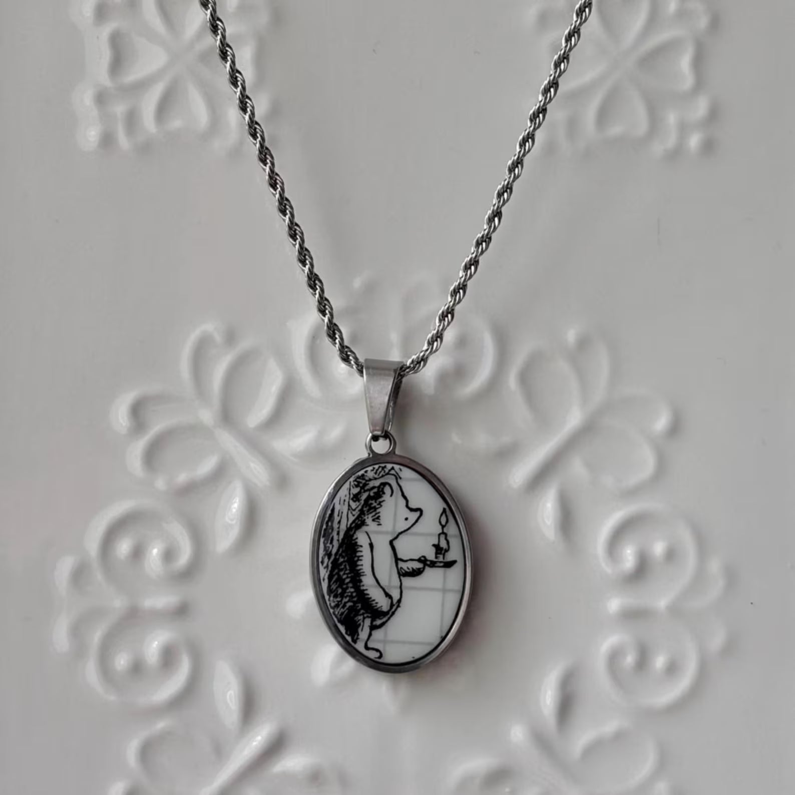 Silver necklace with a pendant featuring a black and white illustration on a textured gray background