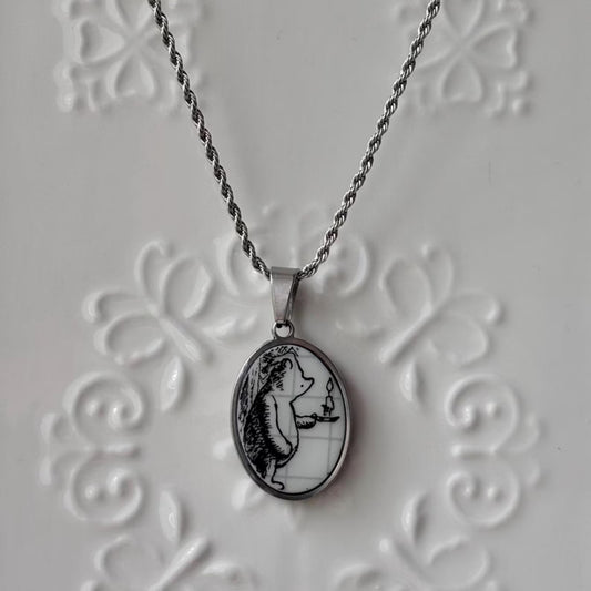 Silver necklace with a pendant featuring a black and white illustration on a textured gray background