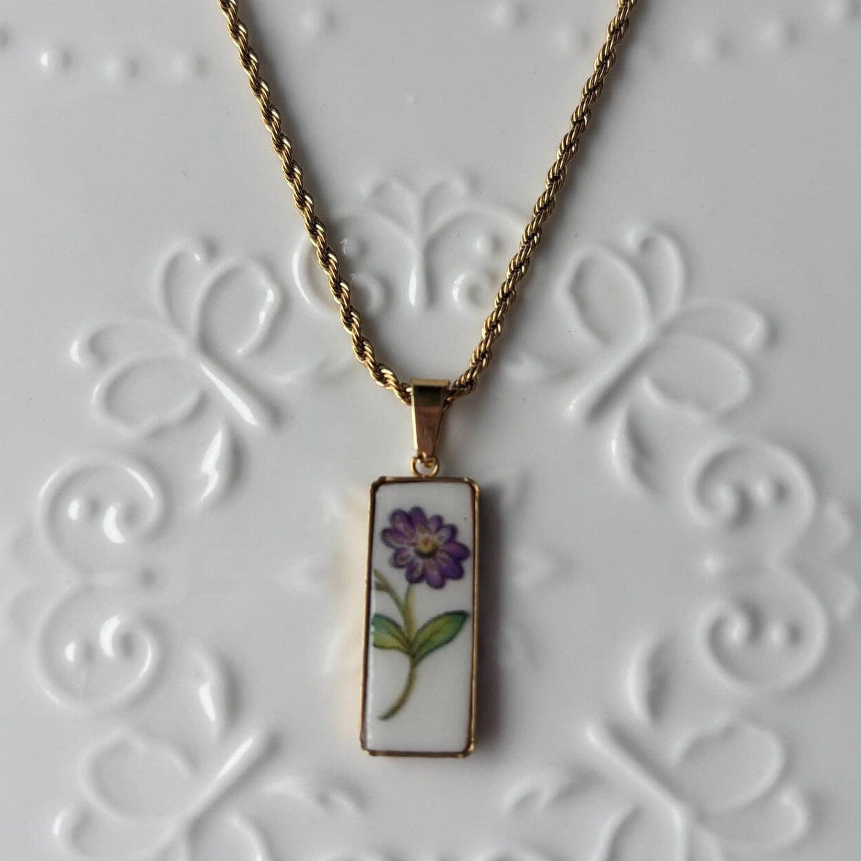 Necklace with a pendant featuring a purple flower design on a textured white background
