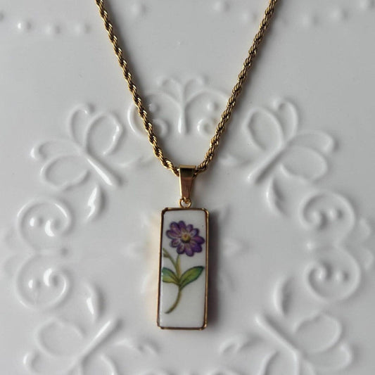 Necklace with a pendant featuring a purple flower design on a textured white background