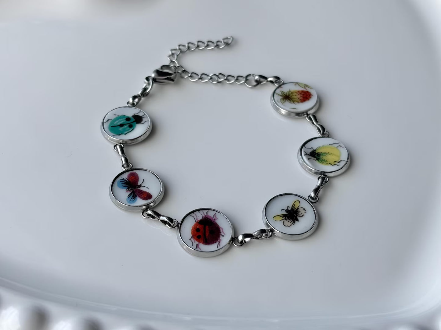 Bracelet with circular charms featuring images of insects on a white plate.